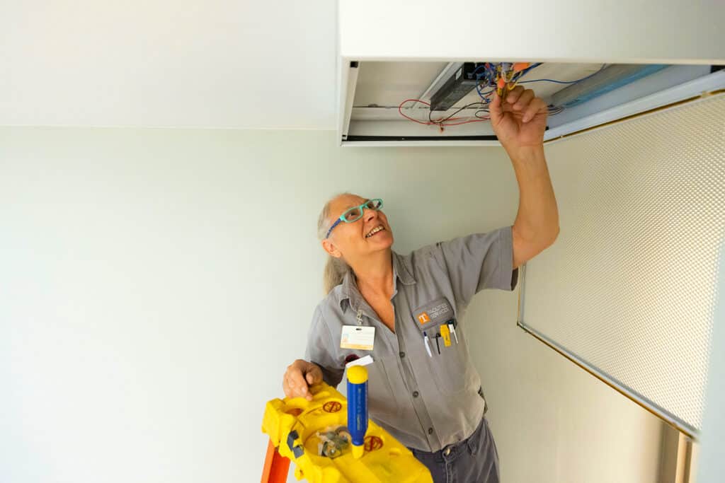 image of a Facilities Services employee on a ladder changing out a ballast in a ceiling light