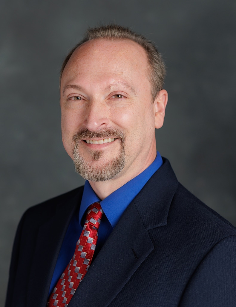 image of Director of Communication and Information Kevin Garland wearing a blue shirt with a red tie and a navy suit jacket
