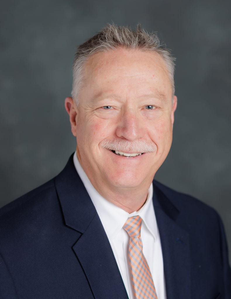 image of Randy Hamilton, Director of Operations, in a white shirt, orange and grey plaid tie, and a navy suit jacket