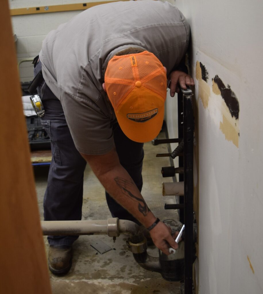 Construction Services team member uses a wrench to complete renovations in a campus facility
