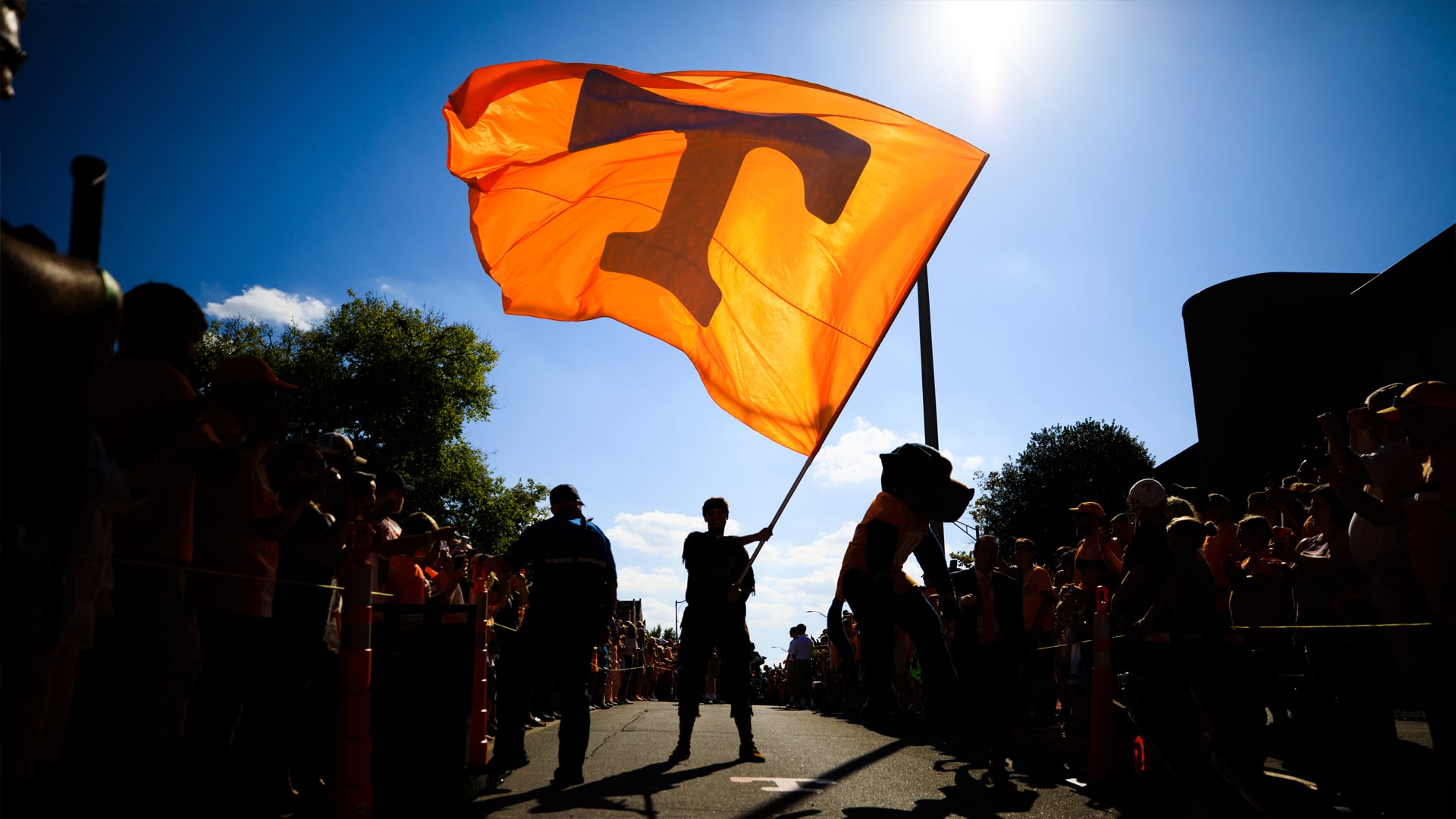 an orange Tennessee Power T flag is waved against a blue sky during the Vol Walk at a UT home football game