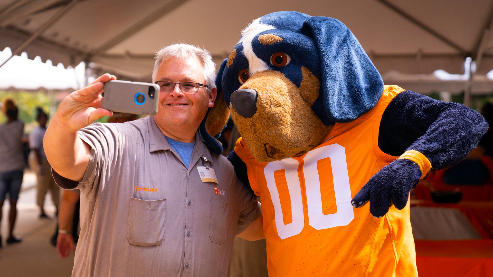 Facilities Services employee poses with costumed dog mascot, Smokey, for a selfie