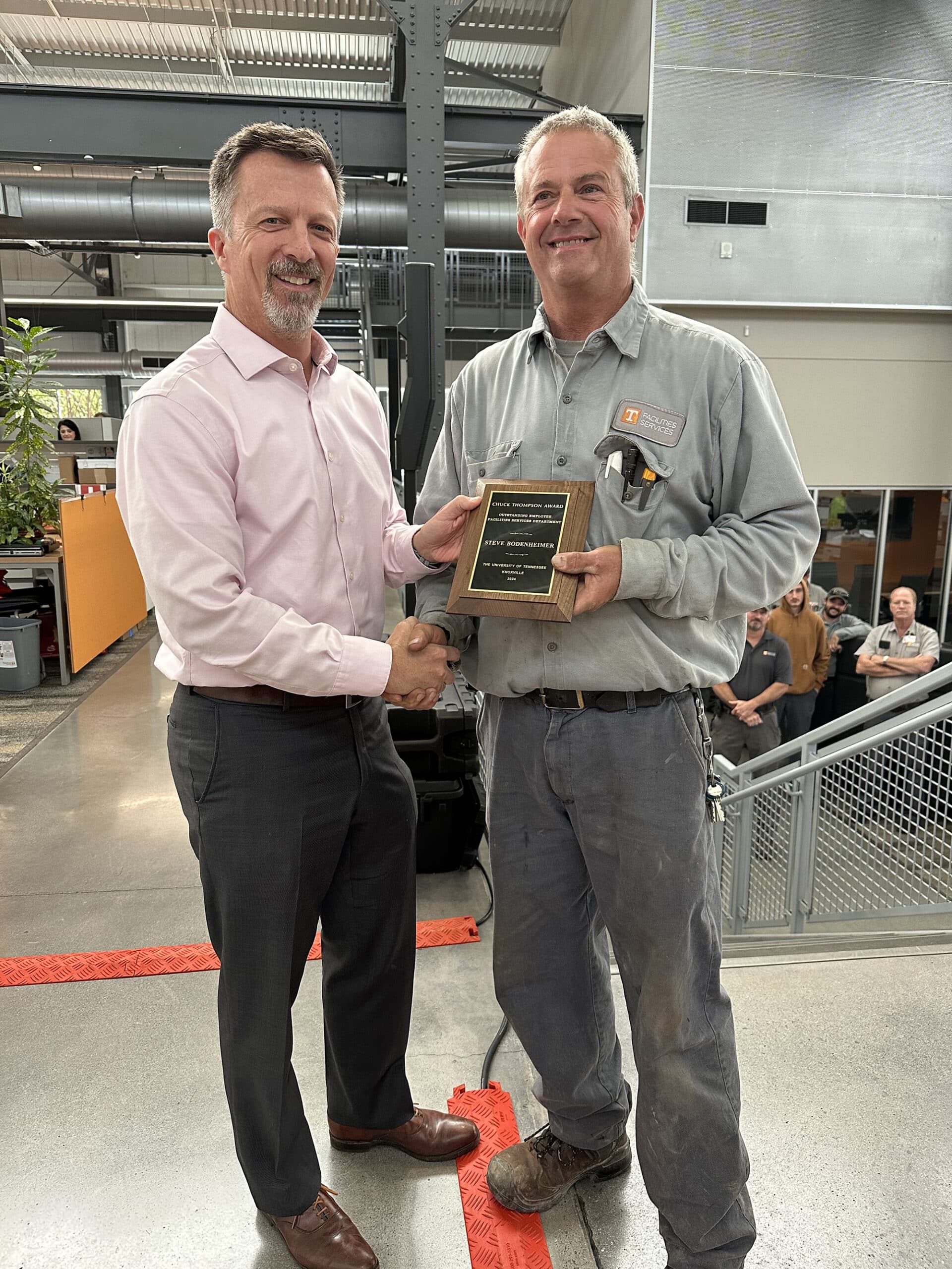 Associate Vice Chancellor Mike Brady hands Steve Bodenheimer the 2024 Chuck Thompson Award for the Crafts services category at the Facilities Services Complex