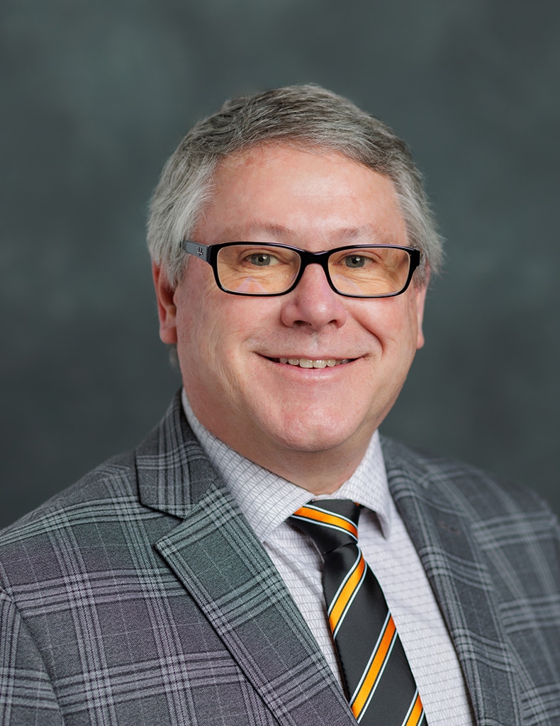 image of Director of Utilities and Energy Wes Willoughby in a white patterned shirt with an orange and black striped die, and a dark grey plaid jacket