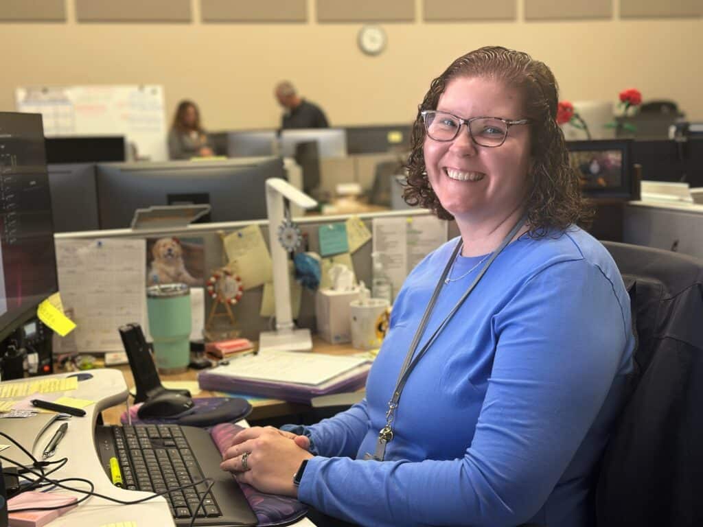 Work Order Management team member Amanda Johnson sits in front of her computer smiling at the camera