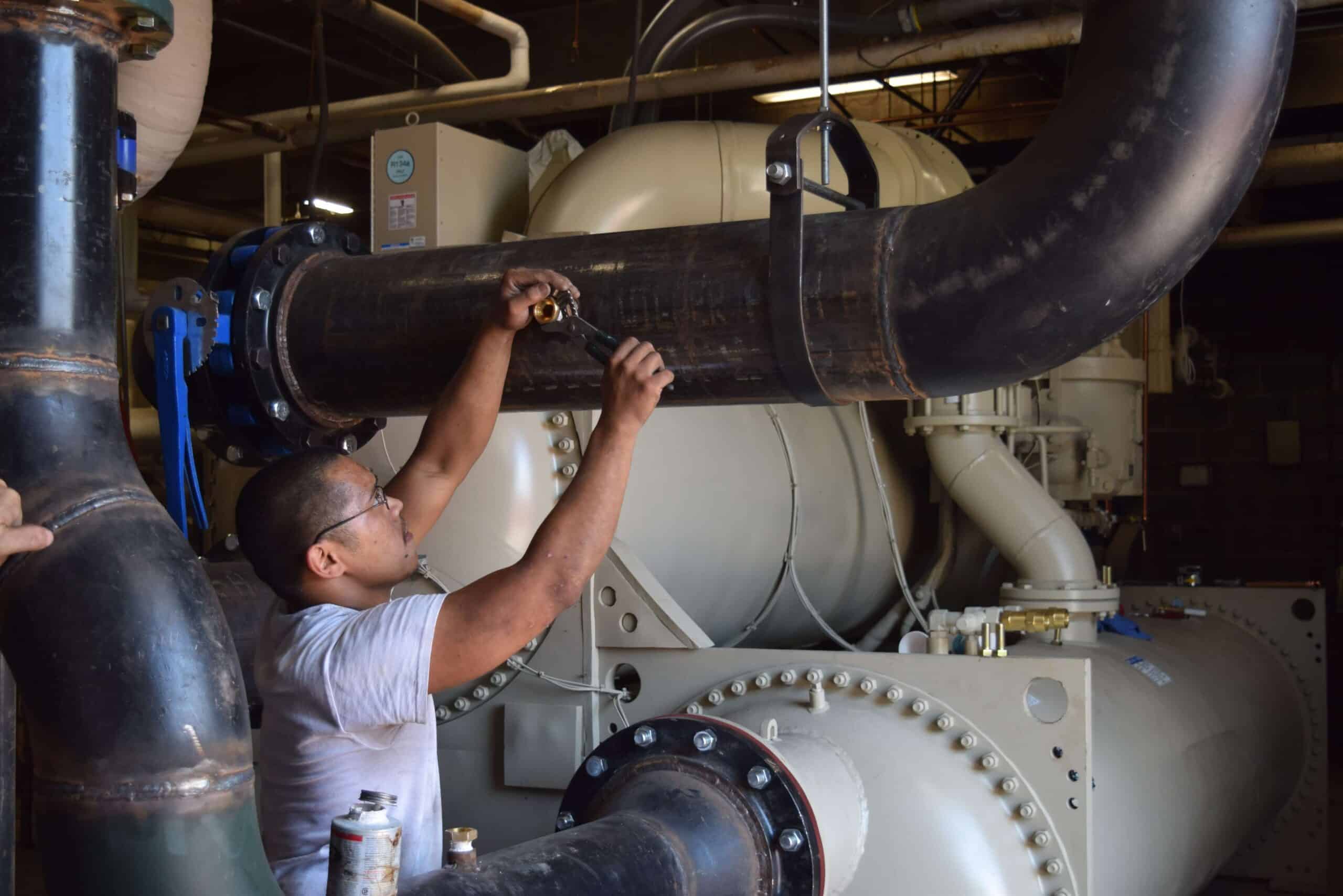 Chris Hinshaw turns a wrench on piping related to a cooling system on campus