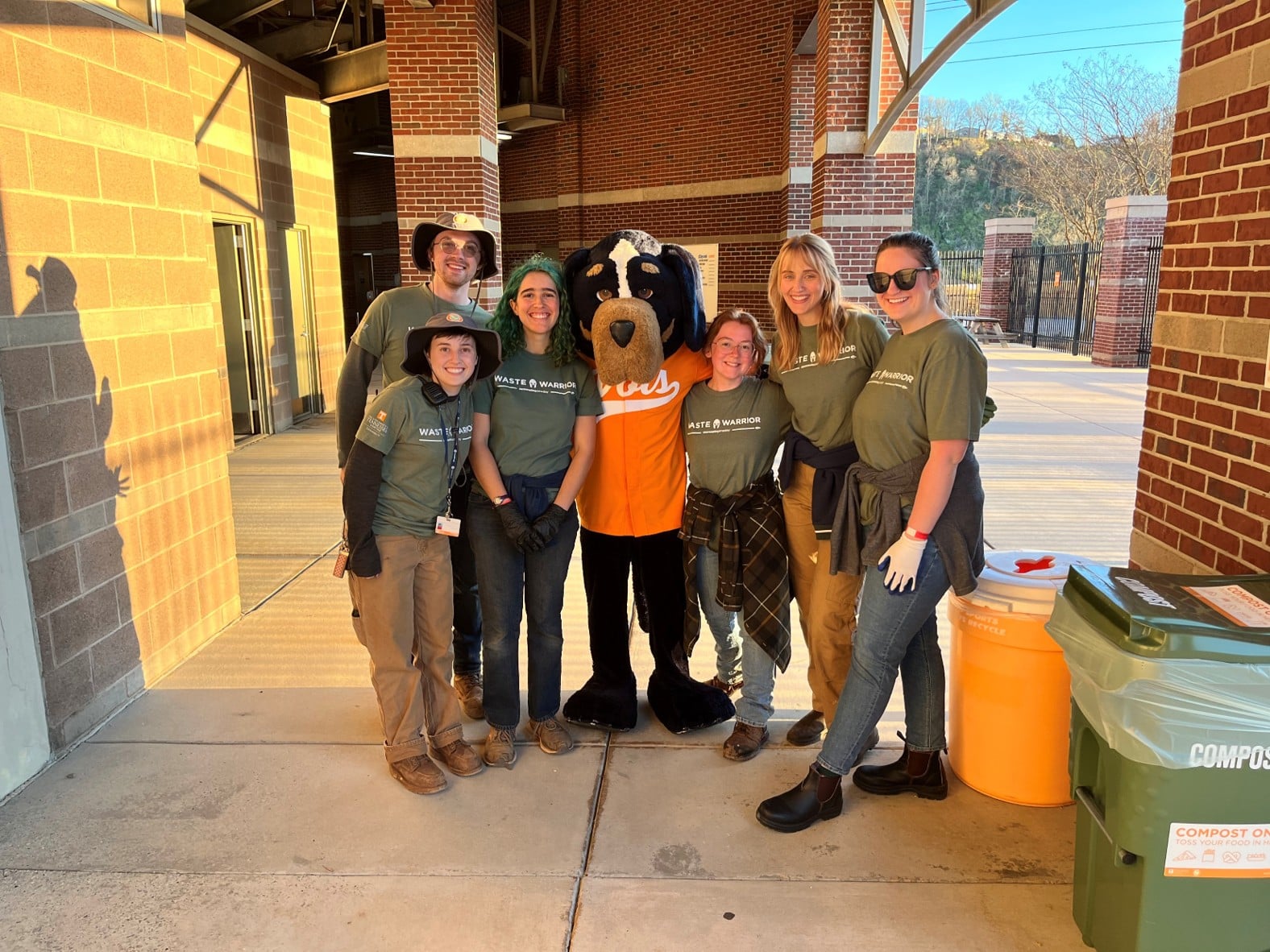 Sustainability team members pose with costume mascot Smokey outside at a Zero Waste Softball event