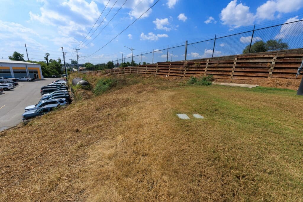 Cleared, dry grassy slope beside a parking area and large building after goat grazing.
