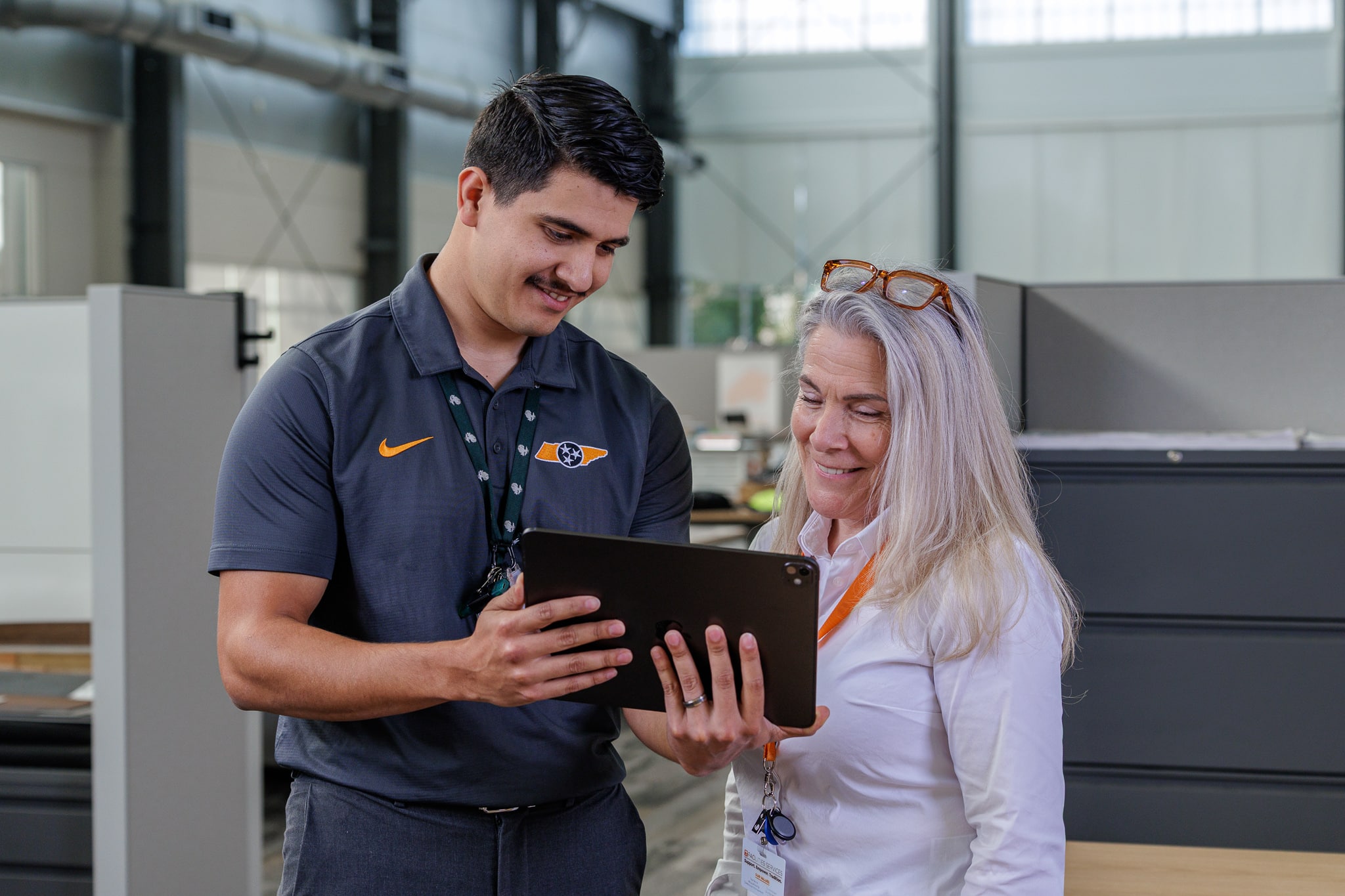 A man and a woman smile while looking at a tablet in an office.